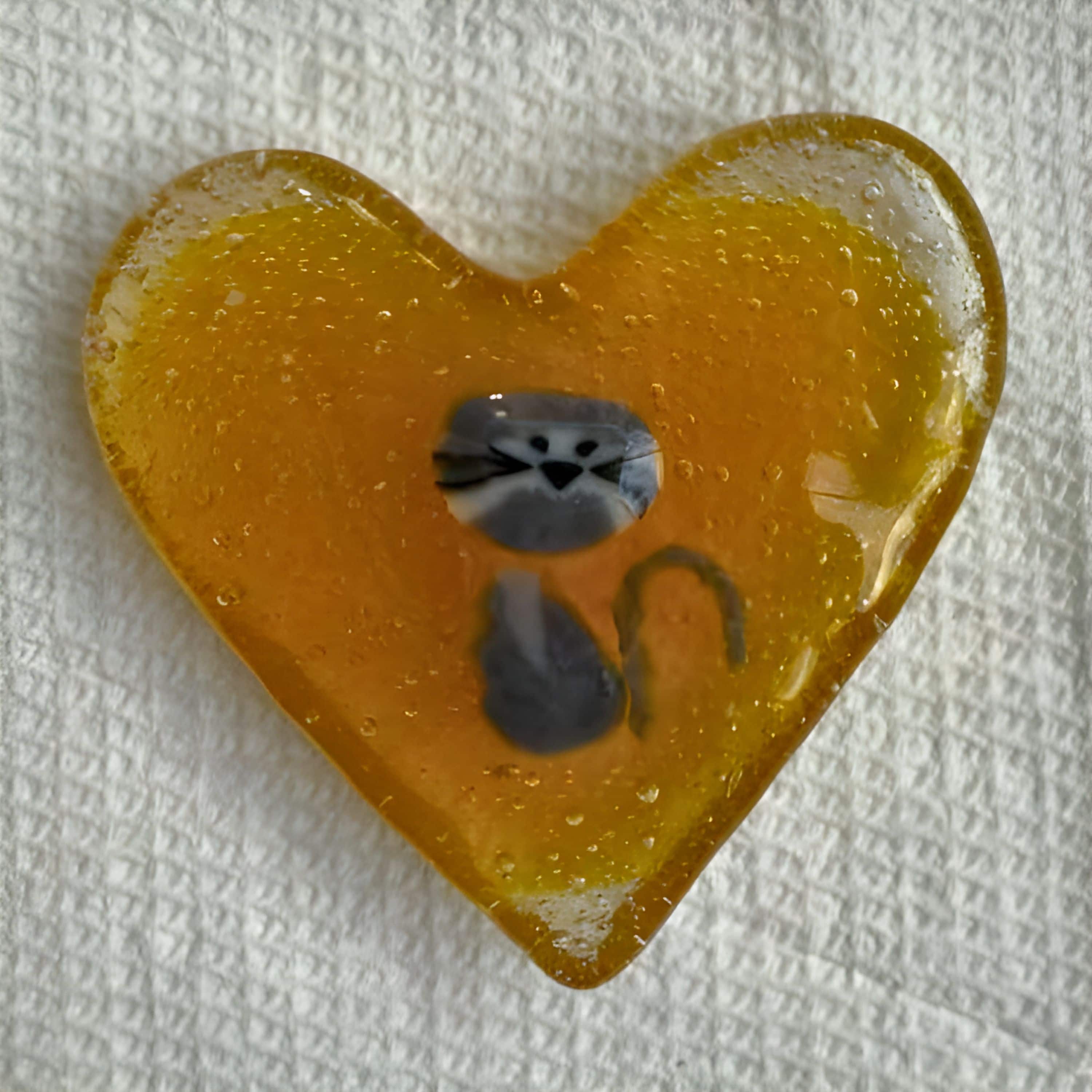 Amber glass heart featuring a whimsical gray cat design embedded inside, created by artist Kathie Brooks Camara.