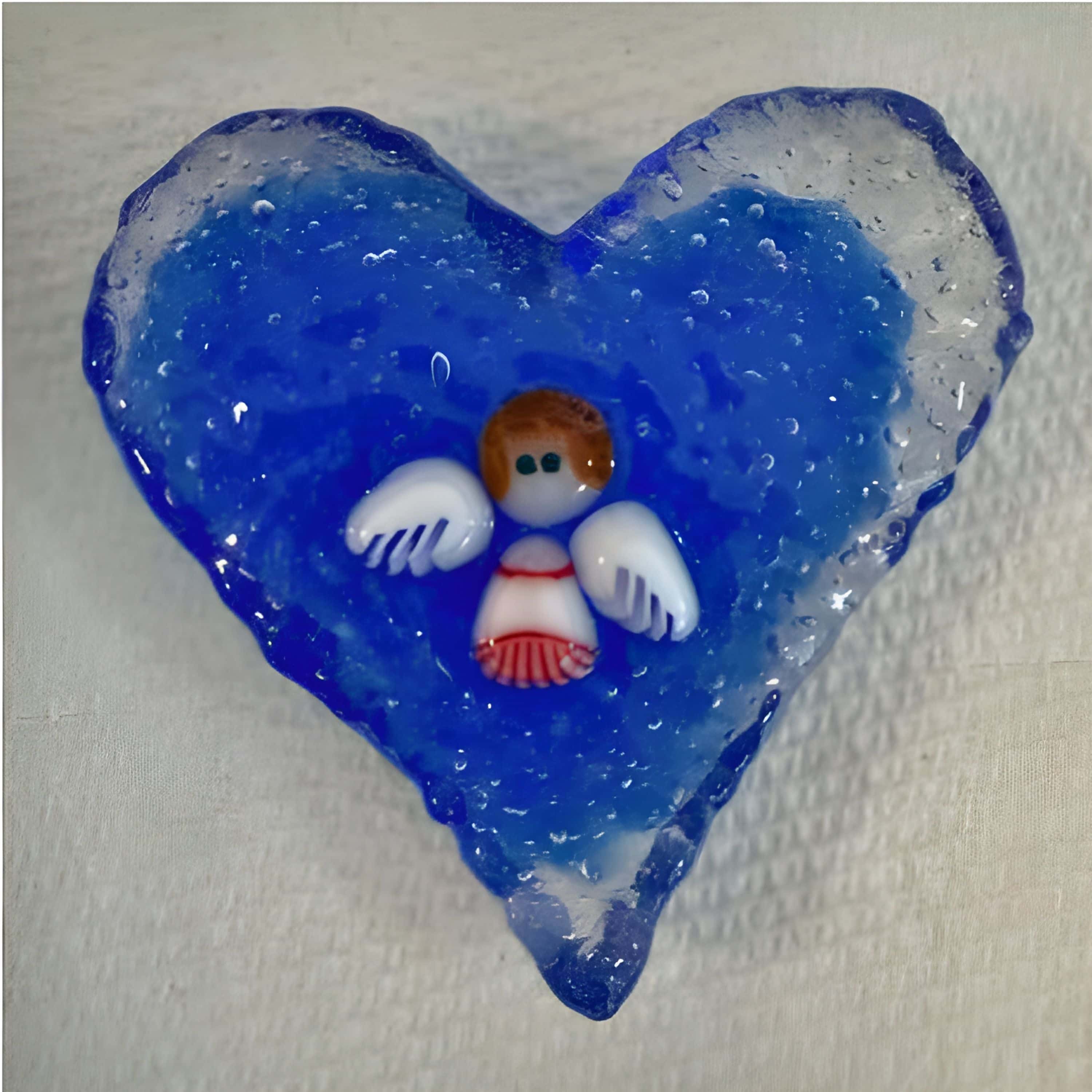 Blue fused-glass heart with a small white-winged angel figure at the center, handmade by Kathie Brooks Camara.