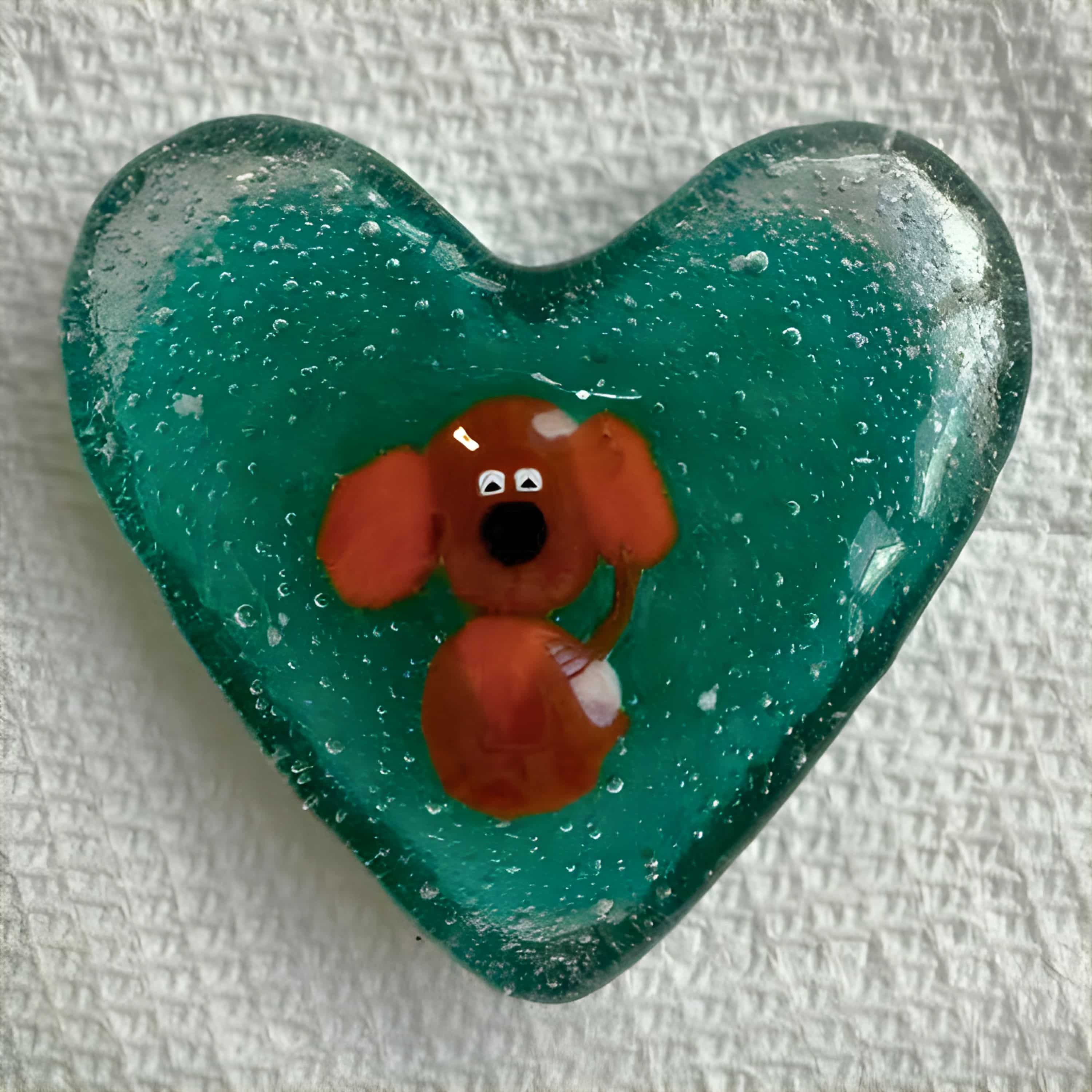 Teal glass heart with an adorable orange dog figure fused inside, crafted by artist Kathie Brooks Camara.