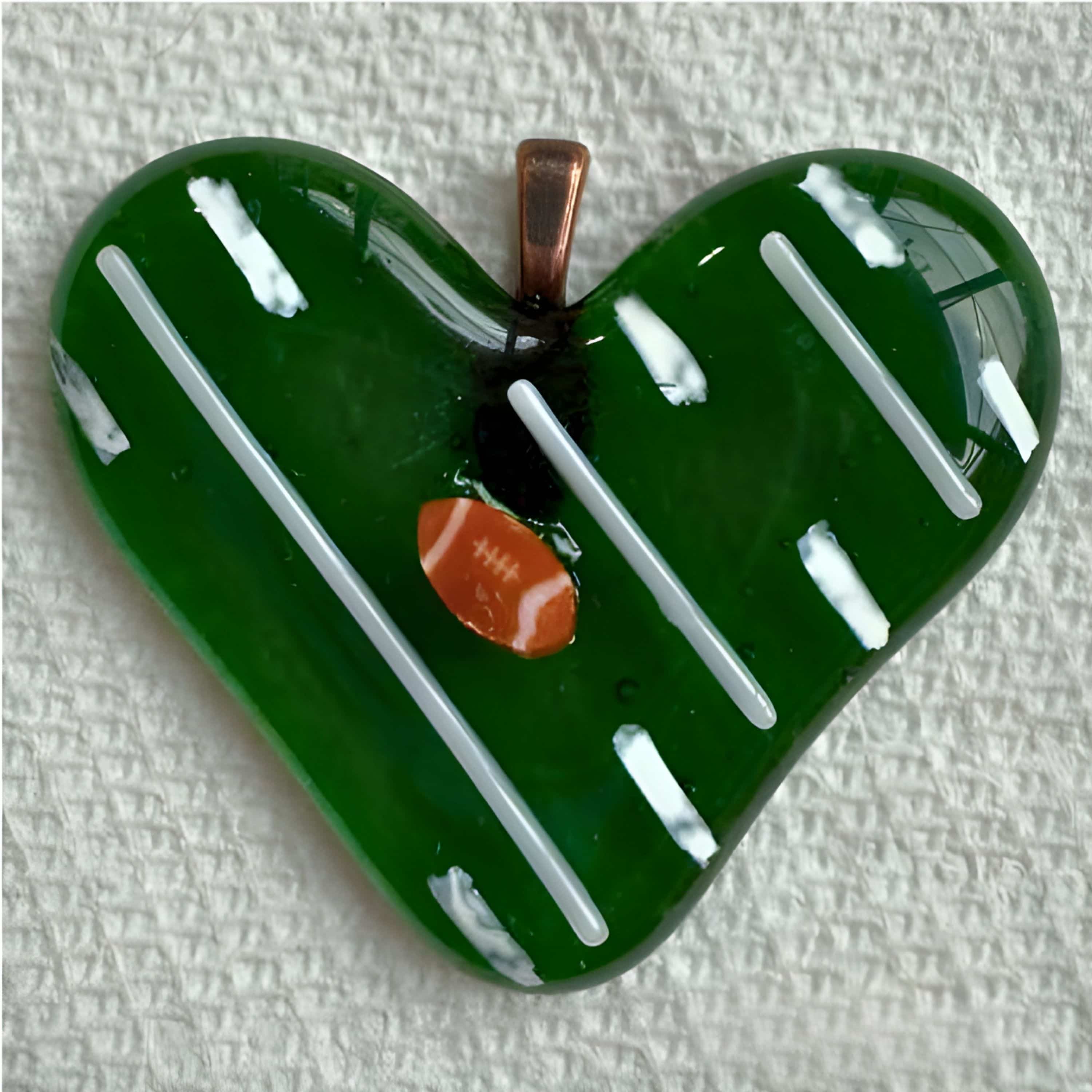 Green fused-glass heart designed to resemble a football field with white yard lines and a tiny orange football, created by Kathie Brooks Camara.